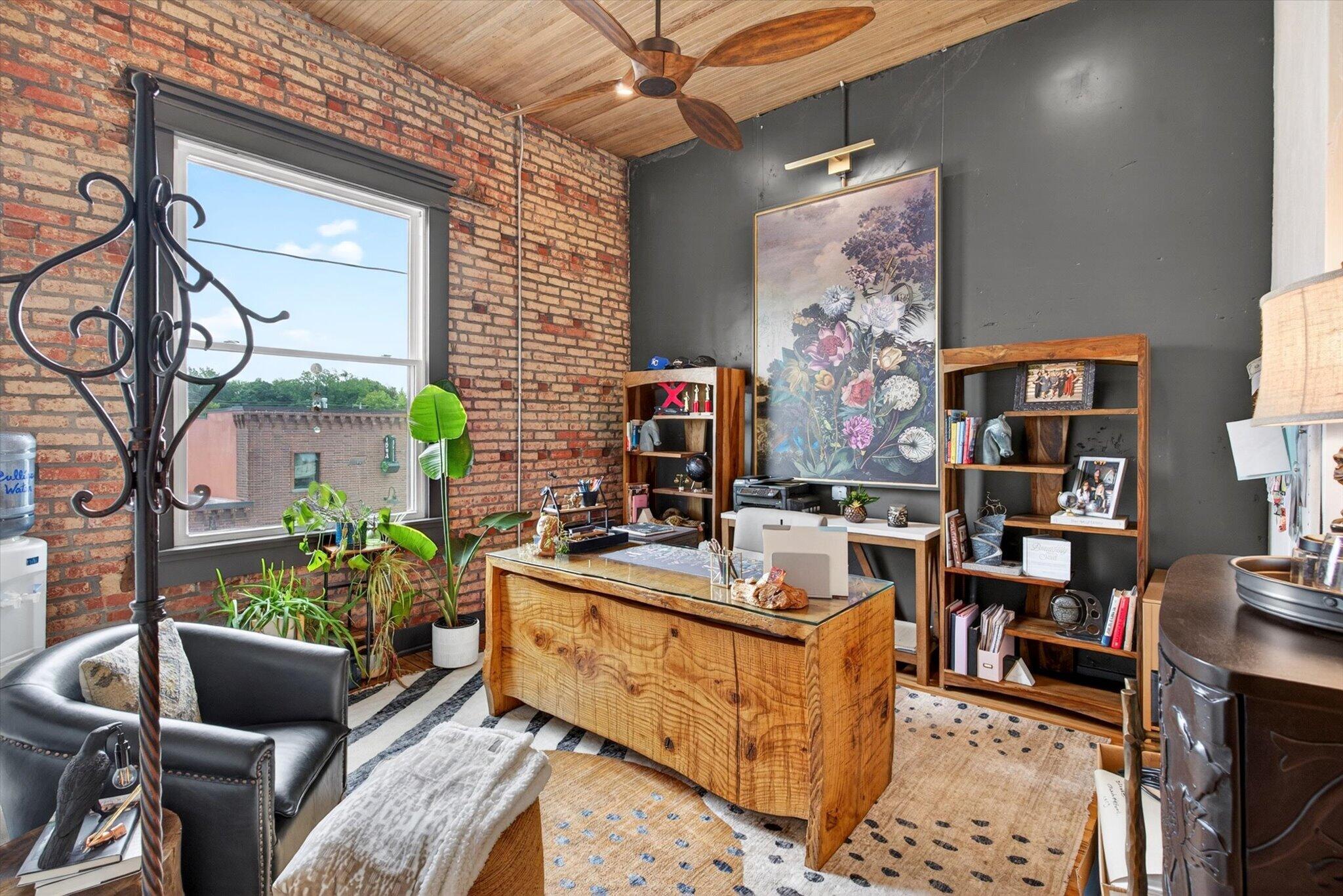 Private office with exposed brick, a wood ceiling, a large window, and a wooden desk